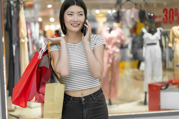 妇女服装店 一位年轻美丽的韩国女人站在商店橱窗边 手里拿着纸袋 与朋友通电话 黑色星期五 — 图库照片