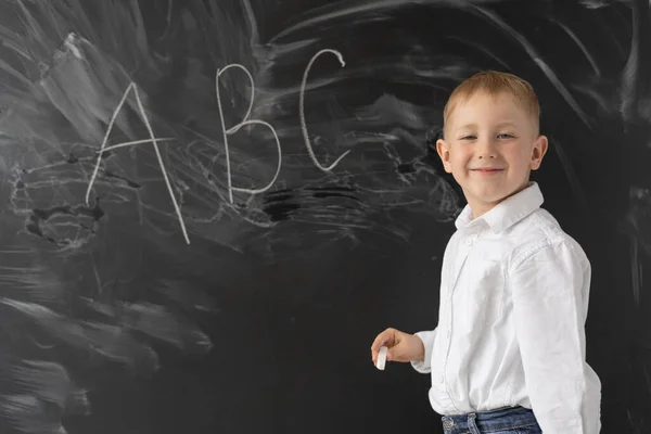 学校に戻るという考えです 小さな男の子が学校の黒板の近くに立っている アルファベットをチョークで書きなさい テキストの場所 — ストック写真