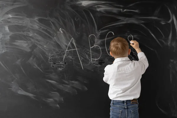 コンセプトは学校に戻ります 少年は黒板にチョークで書きます アルファベットの最初の文字 テキストの場所 ストックフォト