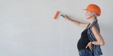 Kafasında turuncu koruyucu miğfer olan genç ve güzel bir kadın müteahhit. Hamile bir kız. Duvarı boya silindiriyle boyuyor. Metin için yer