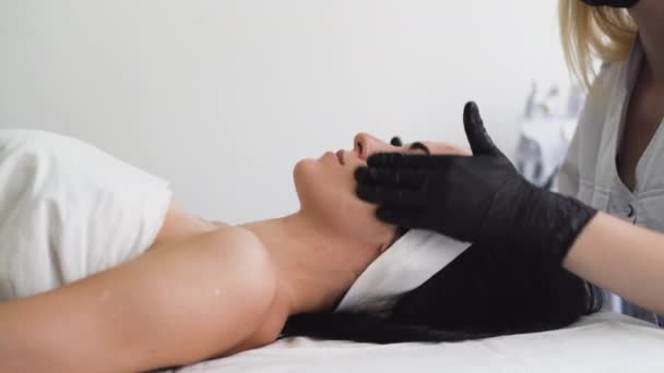 Mulher bonita na recepção de uma esteticista, massagem facial. Procedimento cosmético em um salão de beleza moderno. — Vídeo de Stock