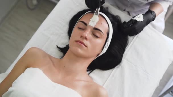 Belle jeune femme à la réception d'une esthéticienne, peau enzymatique peeling. Appliquez un masque blanc sur le visage. Procédure cosmétique dans un salon de beauté moderne. — Video