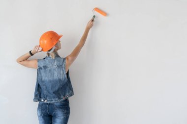 Kafasında turuncu koruyucu miğfer olan kadın müteahhit. Hamile bir kız. Duvarı boya silindiriyle boyuyor. Metin için yer