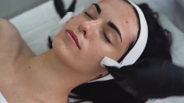 Piękna młoda kobieta w recepcji kosmetyczki, czyszcząca twarz, usuwająca szczątki kremu serwetkami. — Wideo stockowe