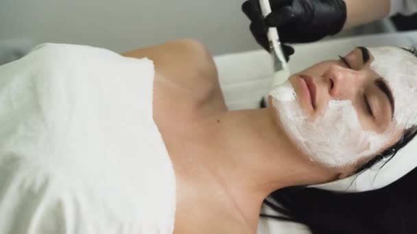 Kosmetyk stosujący peeling enzymatyczny na twarzy kobiet w spa. Stosuje się pędzlem. Zabieg kosmetyczny w nowoczesnym salonie kosmetycznym. — Wideo stockowe