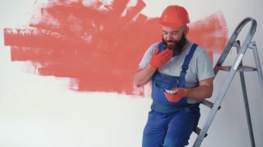 Sakallı bir adam tulum ve koruyucu kask giyiyor. İnşaatçı merdivenlerde oturup para sayıyor. bir yığın 100 'lük banknot