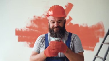 Sakallı bir adam tulum ve koruyucu kask giyiyor. Büyük bir para yığını ellerini kaldırıyor. Duygu Neşe ve gülümseme.