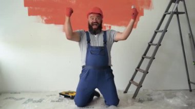 Sakallı bir adam tulum ve koruyucu kask giyiyor. Elinde bir sürü para tutarak dizlerinin üstüne çöker ve kusar. Sevinç ve sevinç duygusu.