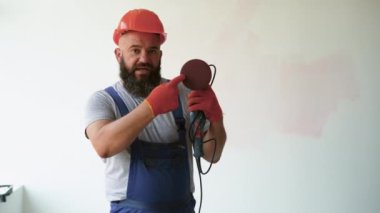 Sakallı bir erkek inşaat işçisi tulum ve koruyucu kask giyer. itici aracın nasıl kullanılacağını açıklayan bir video günlüğü tutar.