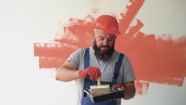 一名留着胡子的男性建筑工人穿着工作服和防护头盔 聚众在刷子上画画 房间里的翻修概念 — 图库视频影像