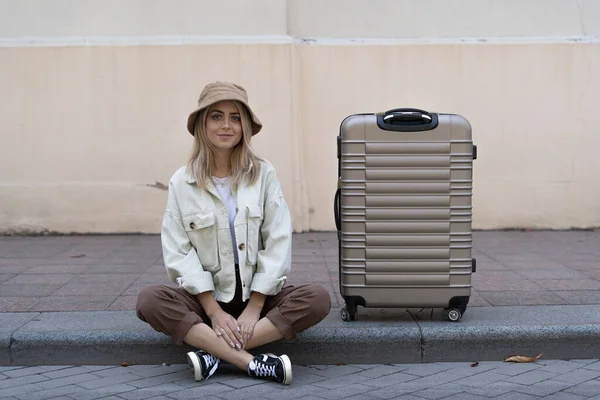 tourist woman with a suitcase in a European city, tourism in Europe. Sits on the sidewalk next to a large suitcase looking at the photographer. Place for text. Copy space.