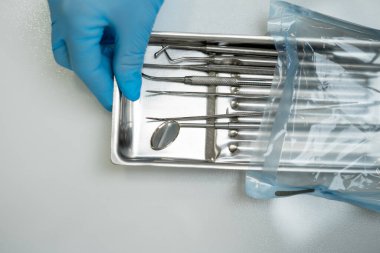 Mavi eldivenli dişçinin ellerinde bir tepsi diş aleti var. Metin için boşluk