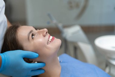 Diş hekiminde check-up bekleyen bir hastanın yakın çekimi. Doktorun elleri yüze yakın.