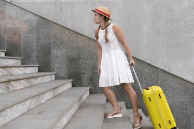 Güzel turist kız seyahat ediyor. Merdivenlerden yukarı büyük sarı bir bavul çıkardı. Boşluğu kopyala.