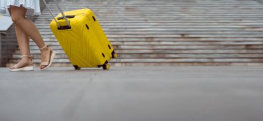 Sokakta bavullu bir kız. Kadın bacakları ve sarı bavul yakın plan..