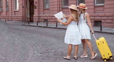 İki güzel ve mutlu turist ellerinde sarı bir bavulla sokakta yürüyorlar. Kadınlar ellerindeki haritaya bakar ve seyahat etmeyi severler..