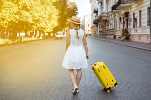 Ένα κορίτσι με κίτρινη βαλίτσα στο δρόμο. οπίσθια όψη της νεαρής γυναίκας. — Φωτογραφία Αρχείου