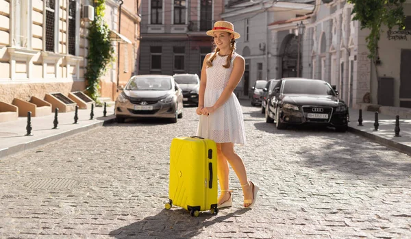 Γυναίκα ταξιδιώτη τουριστική στέκεται με μια κίτρινη βαλίτσα σε ένα δρόμο της πόλης. Η έννοια του ενεργού και τουριστικού τρόπου ζωής. — Φωτογραφία Αρχείου