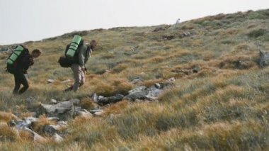İki turist, bir erkek ve bir kadın, dağ yamacında büyük turist çantalarıyla yürüyorlar..