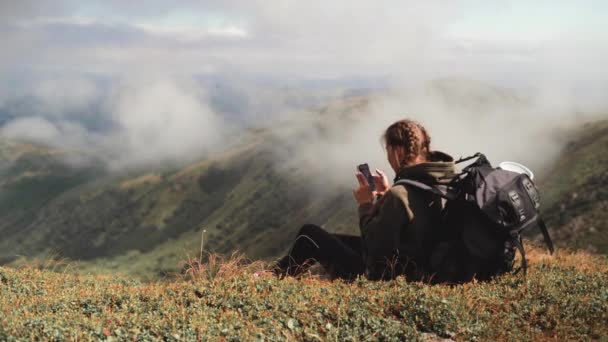 Jovem bela mulher senta-se no topo da montanha e tira uma bela foto em seu telefone — Vídeo de Stock