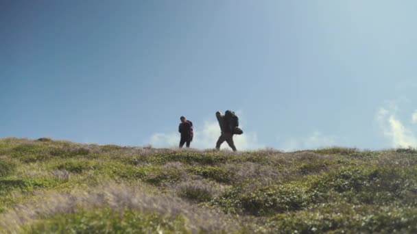 Två turister går längs toppen av kullen med stora ryggsäckar mot himlen — Stockvideo