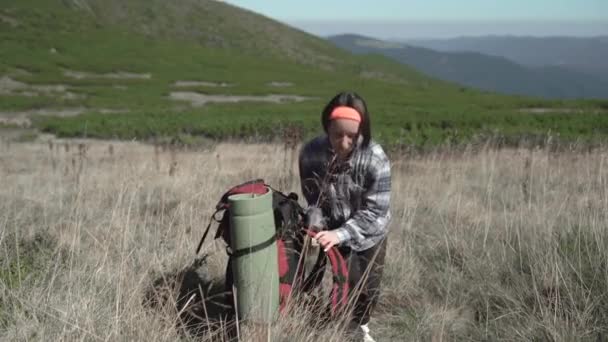 Одна женщина-туристка стоит на вершине горы и кладет рюкзак на плечи. — стоковое видео