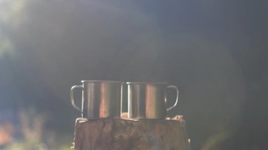 Tahta bir kenevirin üzerinde iki fincan var, bir termos onlardan birine sıcak kahve dolduruyor.