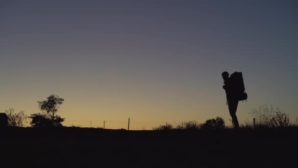 Silhouet van een toerist met een grote rugzak gaat hij van rechts naar links. Wandelconcept — Stockvideo