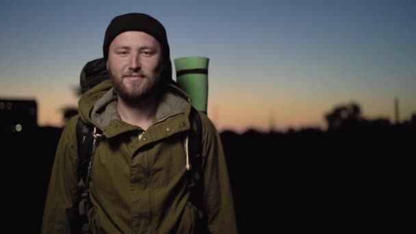 Портрет туриста-мужчины, стоящего на закате, с конфиденциальной улыбкой на лице — стоковое видео