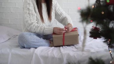 Bir kızın elinin yakın çekimi. Kırmızı kurdeleli bir Noel hediyesi kutusu bağla.