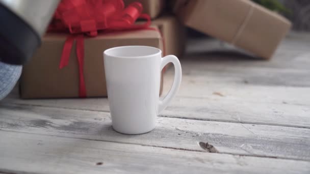 Biały kubek stoi w pobliżu pudełek z prezentami, zalać gorącą wodą z czajnika — Wideo stockowe
