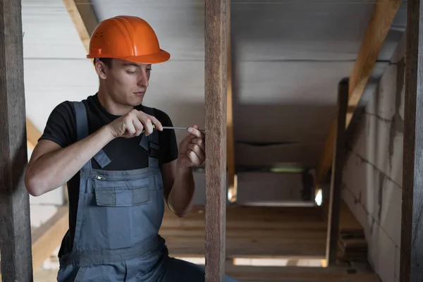 male builder dressed in work clothes and an orange hard hat. tightens a self-tapping screw with a screwdriver. Copy space