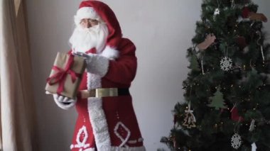 Mutlu Noel Baba 'nın portresi. Noel ağacının yanında duruyor, elinde bir hediye kutusu var.