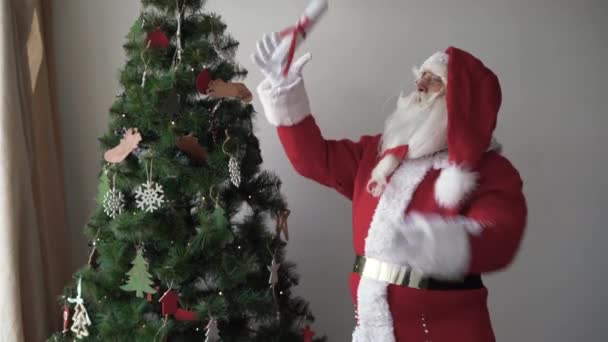 Santa Claus berdiri di dekat pohon Natal, melemparkan selembar kertas dan berteriak padanya seperti megafon — Stok Video