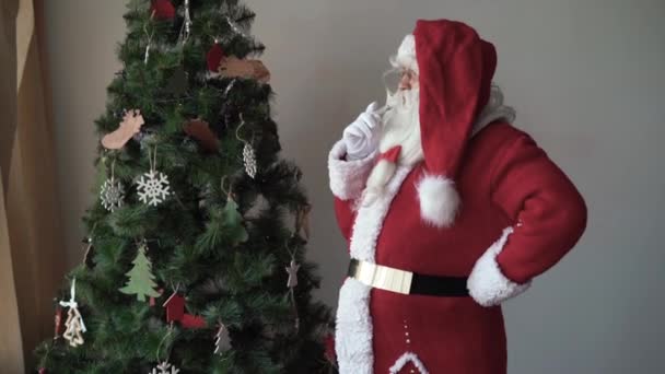 Papai Noel está parado perto da árvore, fumando um cigarro e soprando fumaça — Vídeo de Stock