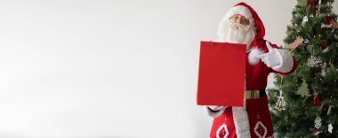 Noel Baba Noel ağacının yanında duruyor, elinde büyük bir alışveriş çantası var. Parmağını ona doğrult. Uyarı