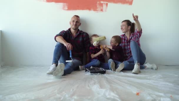 Família de quatro pessoas estão sentadas no chão, descansando. Conceito de renovação de casa — Vídeo de Stock
