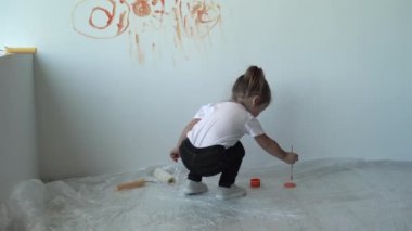 Arkadan bakınca, küçük kız turuncu boyayı alır ve duvara resim yapmaya başlar.