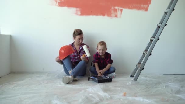 Mãe e filho estão sentados em casa no chão, descansando depois de pintar as paredes. Conceito de renovação de casa — Vídeo de Stock