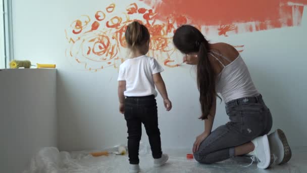 Mamma och dotter sitter på golvet nära väggen. Måla med orange färg — Stockvideo