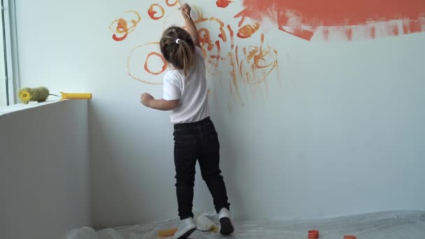 Vista trasera, una niña está cerca de una pared blanca y pinta con pintura naranja — Vídeo de stock