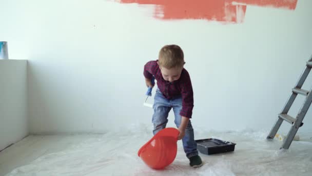 Liten pojke lyfter upp en orange skyddshjälm sätter den på huvudet — Stockvideo