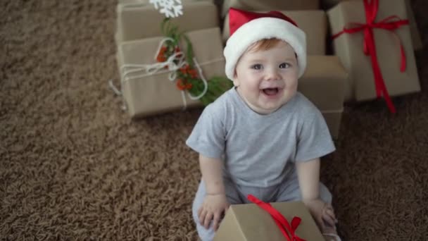 Little child in santa claus hat smiles cheerfully. dog jack russell licks him. Many boxes with gifts — Stock Video