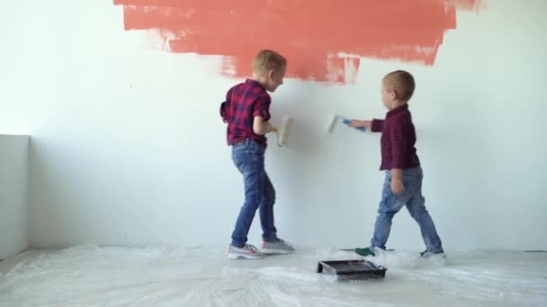 Två barn pojkar måla väggen med rullar. Renoveringskoncept för hemmet — Stockvideo