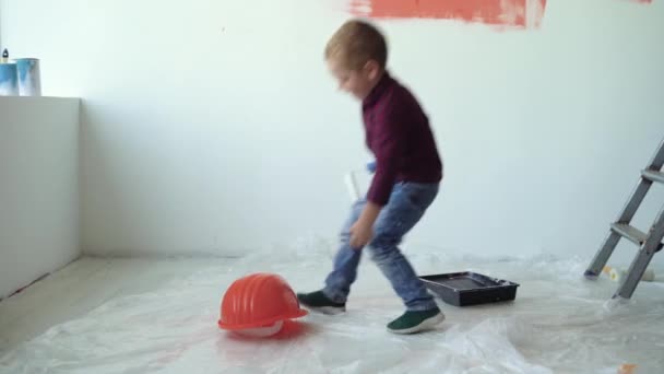 Un niño pequeño levanta un casco protector naranja en su cabeza. Concepto de renovación del hogar — Vídeos de Stock