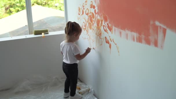 Una niña se para cerca de la pared y dibuja con un pincel. Pintura naranja — Vídeo de stock