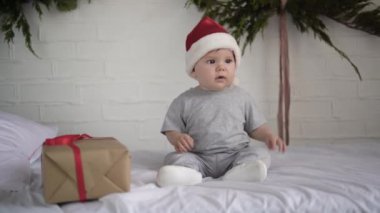 Küçük çocuk yatakta Noel Baba şapkası takıyor. Hediye kutusu