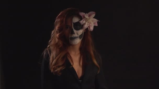 Porträtt av en ung kvinna med makeup för Halloween på en mörk bakgrund. en ljusstråle dyker upp och försvinner — Stockvideo
