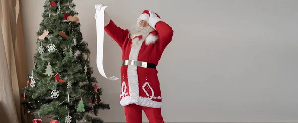 Święty Mikołaj Ubrany Czerwony Garnitur Stoi Blisko Choinki Patrz Wielką — Zdjęcie stockowe