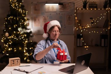 Noel arifesinde klinikte gece vardiyasında bilgisayarla çalışırken hemşire ya da doktor kırmızı hediye paketini açıyor. Sağlık ve Tıp Konsepti